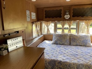 A bedroom with a bed, a bedside table, a lamp, a window with curtains, and a sign on the wall. - Sweet Camper Ideal for a Romantic Escape in Gatlinburg, Tennesse (Gatlinburg)