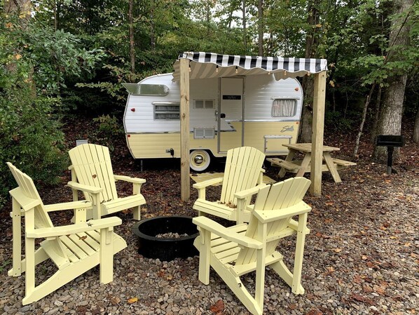 A recreational area with a trailer, Adirondack chairs, and a fire pit. - Sweet Camper Ideal for a Romantic Escape in Gatlinburg, Tennesse (Gatlinburg)