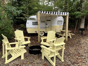 Ein Erholungsbereich mit einem Wohnwagen, Adirondack-Stühlen und einer Feuerstelle.