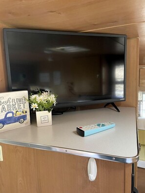 A television mounted on a wall with a remote control and a small potted plant beside it. - Sweet Camper Ideal for a Romantic Escape in Gatlinburg, Tennesse (Gatlinburg)