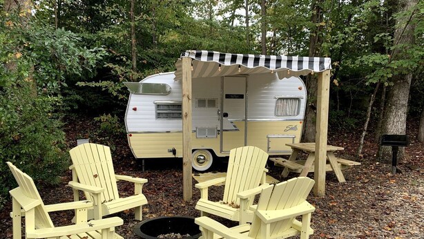 Un espacio recreativo con una caravana, sillas Adirondack y un brasero.