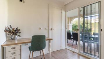 Une pièce avec un bureau en bois, une chaise verte, une plante en pot et une porte-fenêtre coulissante donnant sur un patio extérieur.