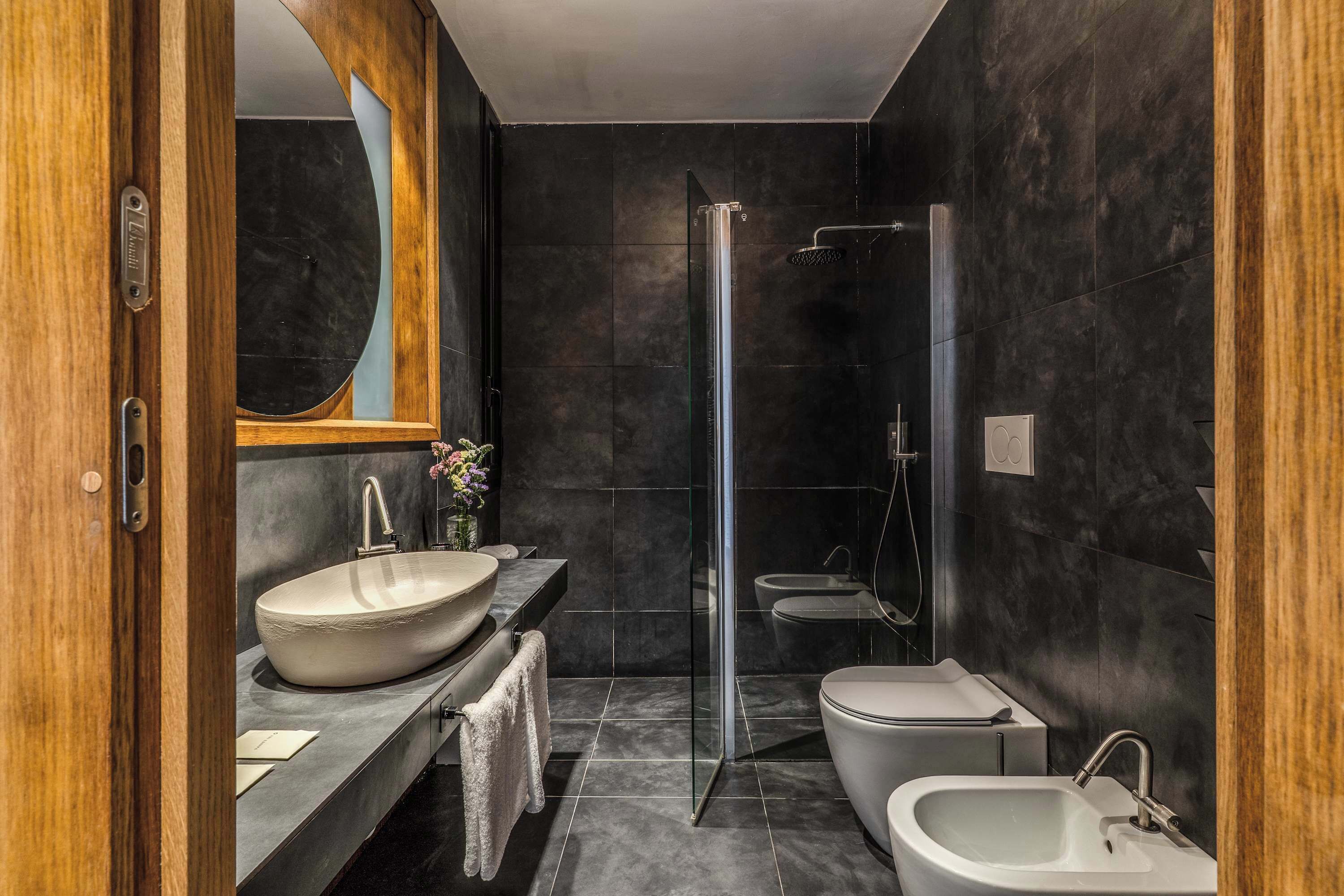 Une salle de bain moderne dotée d’un grand lavabo sur pied, d’une baignoire îlot, d’une douche à parois de verre et d’un miroir encadré en bois.