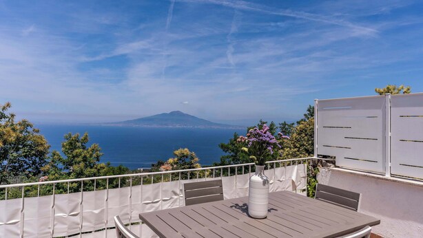 A balcony with a table and chairs, a vase with flowers, and a view of the sea and a mountain. - Sea View Suite Priora with Private Terrace (Priora)