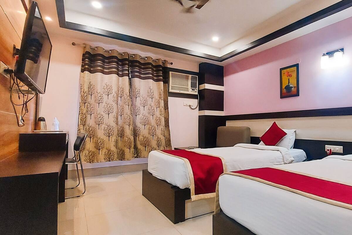 Habitación de hotel con dos camas, televisor, escritorio y ventana con cortinas.