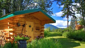 A wooden cabin with a green roof, a sign reading 'SAUNA,' and a log pile outside. - Historic Cozy Off-Grid Cabin with Creekside Steam Sauna near Log Cabin Creek, Tok, Alaska (Tok)