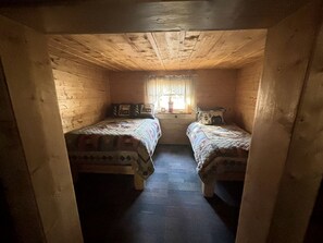 Una habitación pequeña y acogedora con dos camas, una ventana con cortinas y techo de madera.
