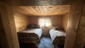 A small, cozy room with two beds, a window with curtains, and a wooden ceiling. - Historic Cozy Off-Grid Cabin with Creekside Steam Sauna near Log Cabin Creek, Tok, Alaska (Tok)