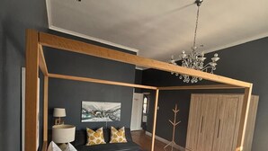 A modern bedroom with a four-poster bed, a chandelier, a wardrobe, and a painting on the wall. - Herbert House (Cape Town)