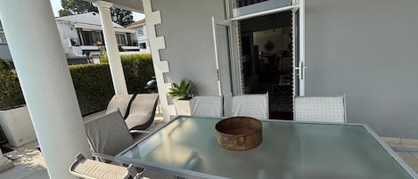 An outdoor patio with a glass table, four chairs with patterned cushions, and a rustic bowl on the table.