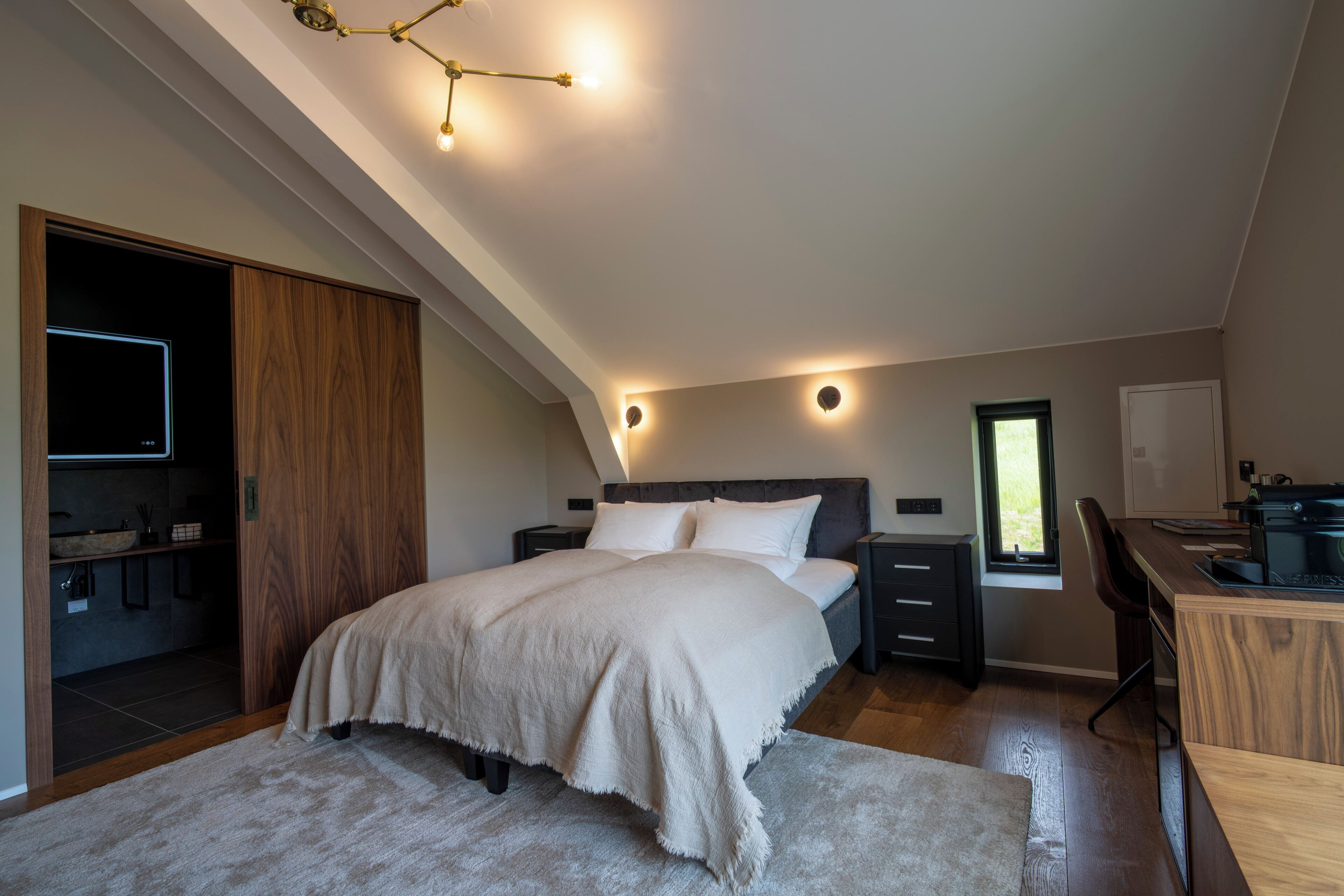 A bedroom with a bed, bedside tables, a desk, a window, and a built-in wardrobe.