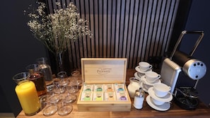 Una preparación para el desayuno con una caja de té Pickwick, tazas, platillos, una cafetera y una vela.