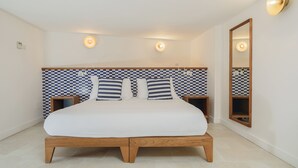 Un dormitorio con pared a cuadros, cama con ropa de cama blanca, dos mesitas de noche y un espejo en la pared.