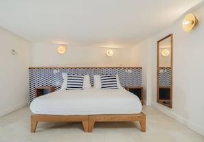 Un dormitorio con pared a cuadros, cama con ropa de cama blanca, dos mesitas de noche y un espejo en la pared.