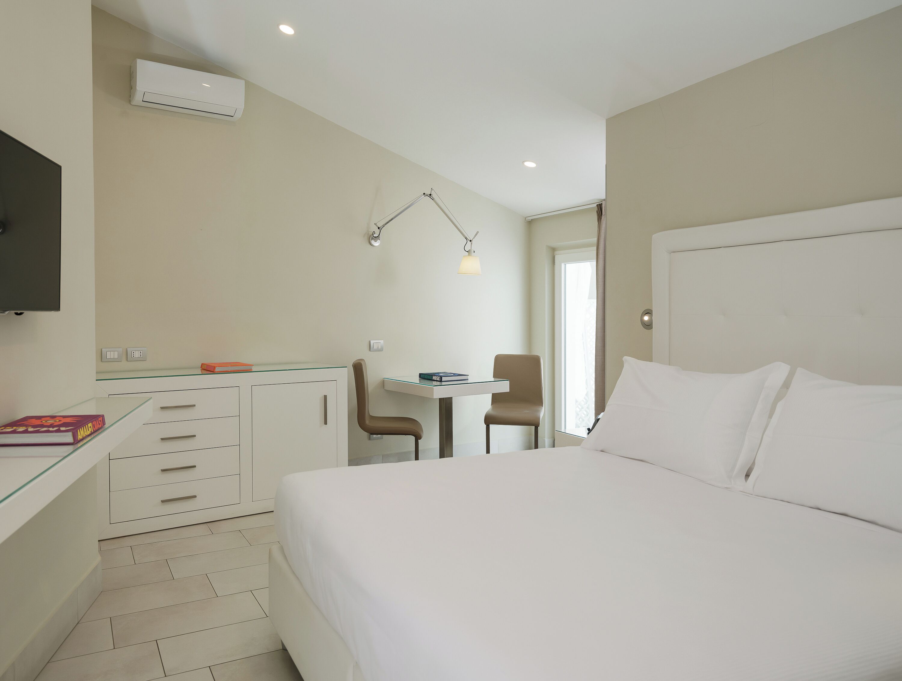 Ein Hotelzimmer mit einem Bett, einem Schreibtisch mit Stuhl, einem Fernseher und einem Fenster.
