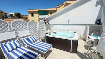 Una terrassa al terrat amb seients de relaxació, un bany d'hidromassatge i vista dels edificis veïns.