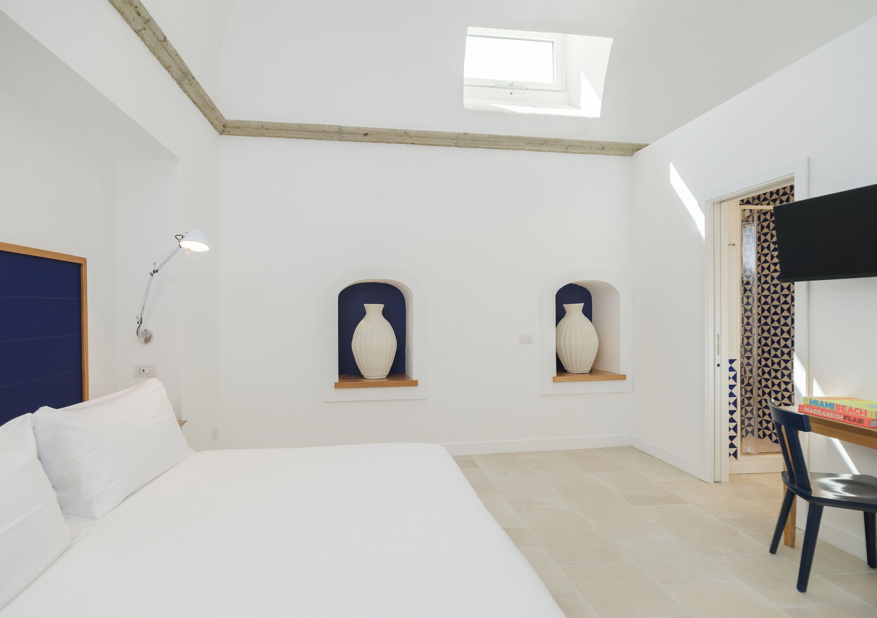 Une chambre à coucher avec un lit, deux vases fixés au mur, un bureau avec une chaise et une porte ornée de rideaux à motifs.