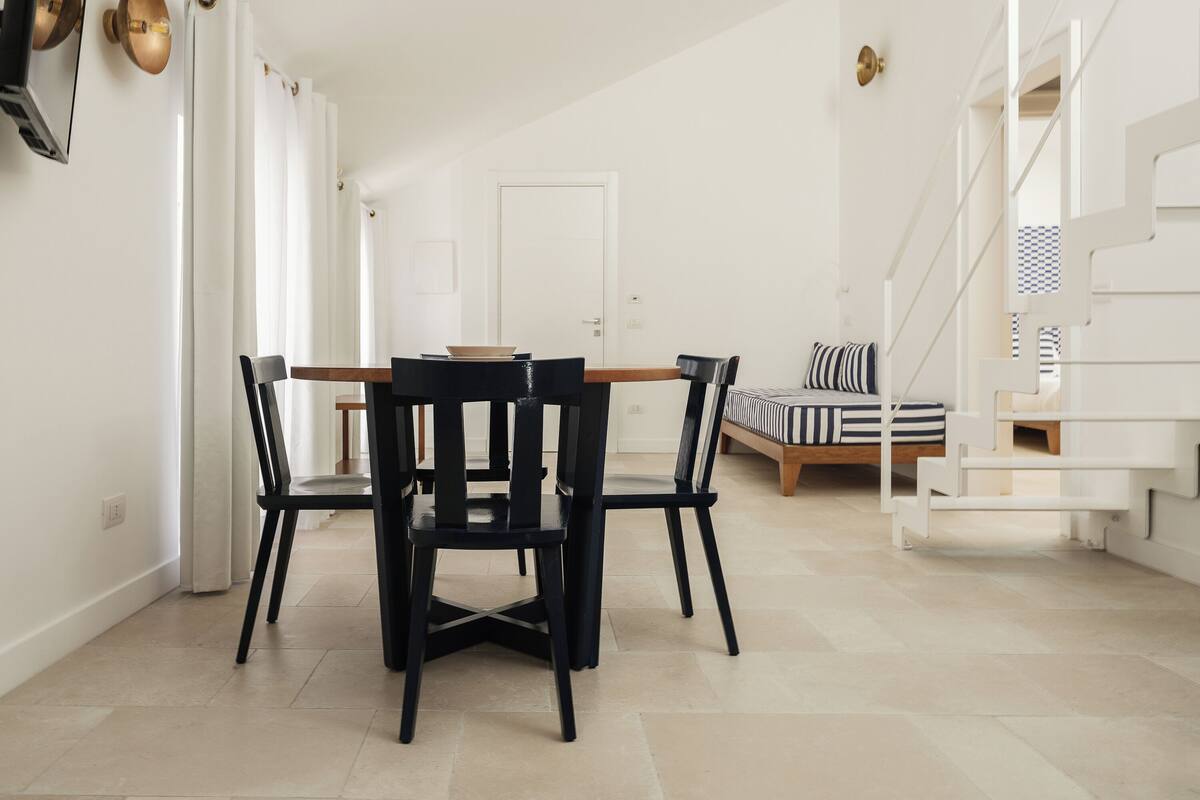 A modern interior with a dining area, a staircase, and a bed.