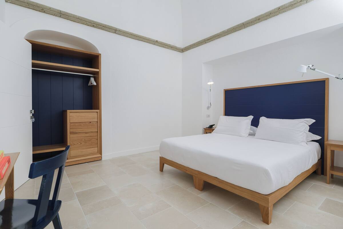A bedroom with a bed, wooden wardrobe, and a desk with chair.