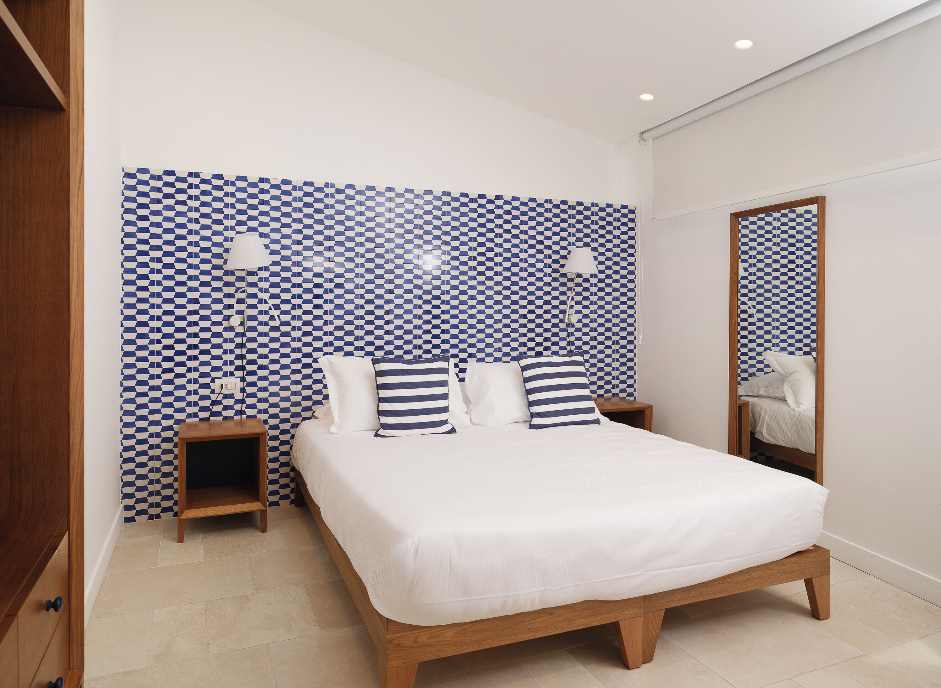 Un dormitorio con pared a cuadros azules y blancos, un cabecero de madera, dos mesitas de noche y un espejo.