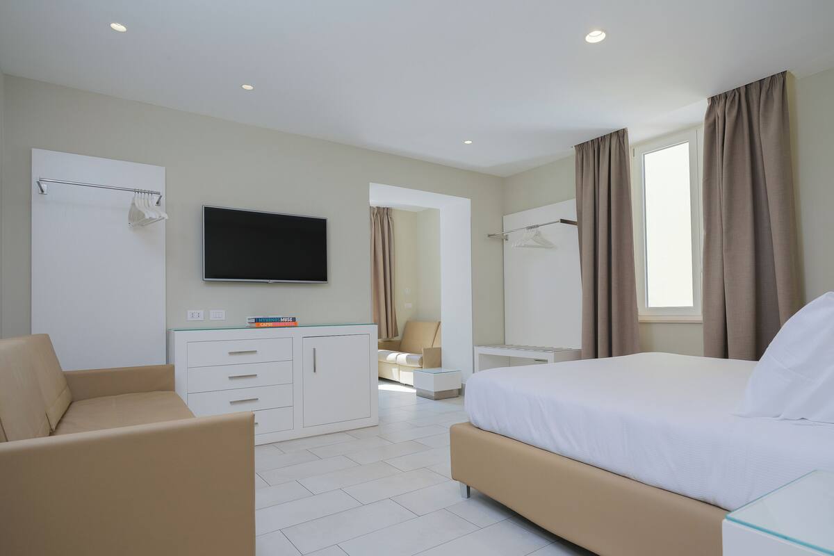 A hotel room with a bed, a desk with a flat-screen TV, a chair, and a wardrobe.