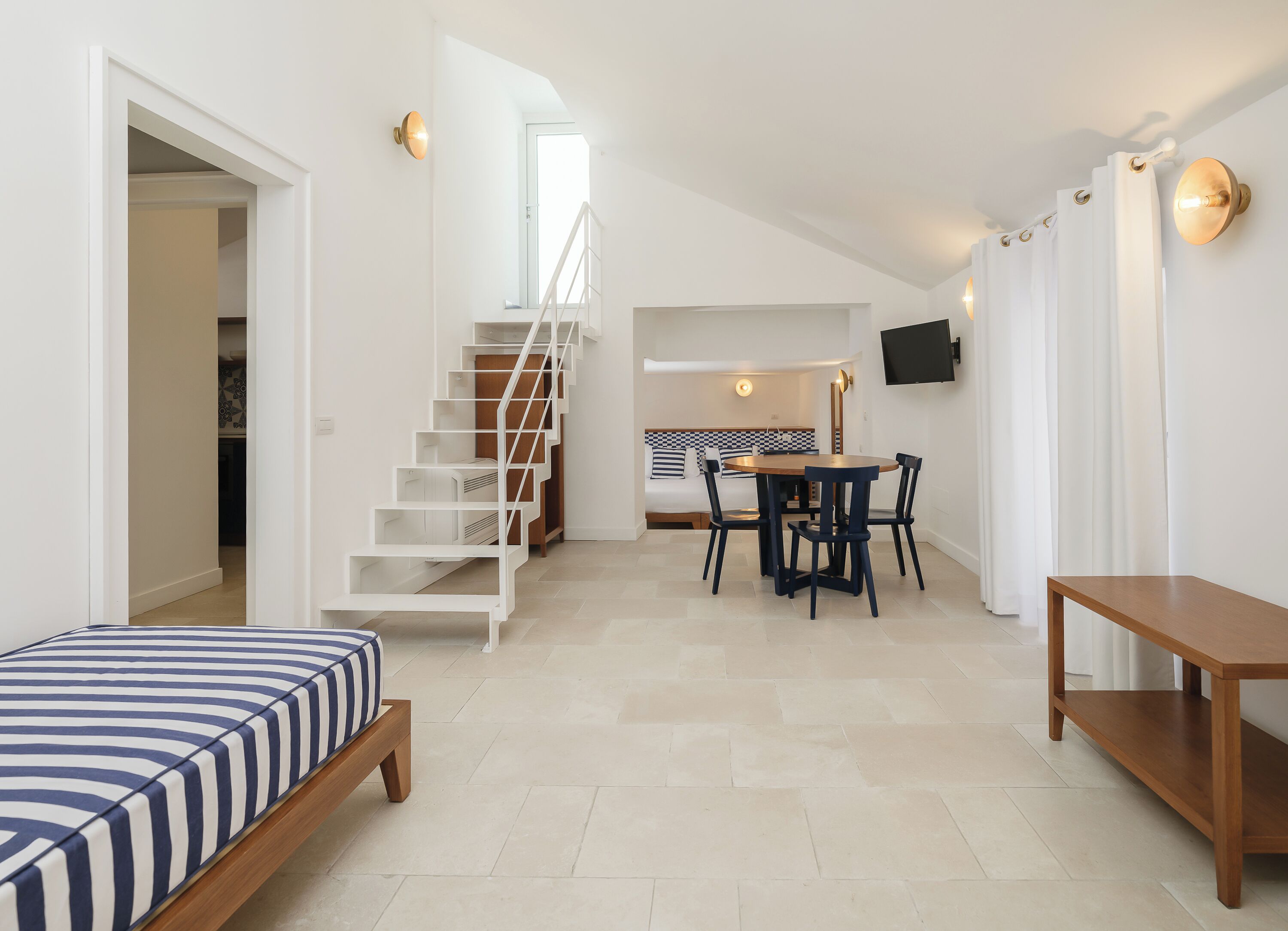 Un espacio habitable pequeño con una cama, una mesa de comedor con sillas, una escalera y un televisor montado en la pared.