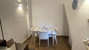 Un área de comedor con una mesa y sillas, una escalera y una lámpara fijada a la pared.