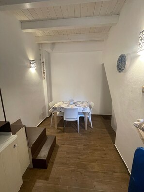 A dining area with a table and chairs, a staircase, and a wall-mounted light fixture. - Romantic Cefalù - Studio Apartment in the Heart of the Historic Center (Cefalù)