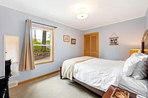 Ein Schlafzimmer mit Bett, einem Fenster mit Vorhängen, einem Holzschrank und einer Nachttischlampe.