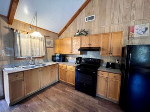 Una cocina con armarios de madera, una estufa negra, un microondas y un refrigerador.