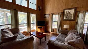 A spacious living room with two sofas, a coffee table, a television, and large windows with curtains.