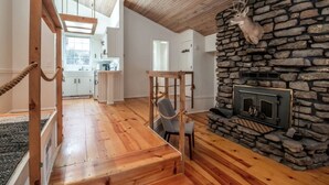Ein geräumiges Wohnzimmer mit Kamin aus Stein, Holzböden und Blick zur Küche.