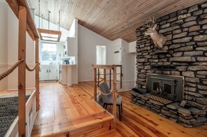 Ein geräumiges Wohnzimmer mit Kamin aus Stein, Holzböden und Blick zur Küche.