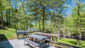 Ein Picknickplatz mit Grill, Bänken und einer Holzterrasse mit Blick auf einen bewaldeten Bereich.