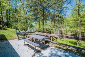 A picnic area with a grill, benches, and a wooden deck overlooking a forested area. - Newly Remodeled Cabin with Lake Views & Grill Patio in Rogers, Arkansas (Rogers)