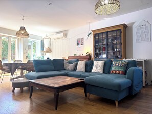 Ein Wohnzimmer mit einem Ecksofa, einem Couchtisch, einer Pendelleuchte, einer Vitrine und einer wandmontierten Klimaanlage.