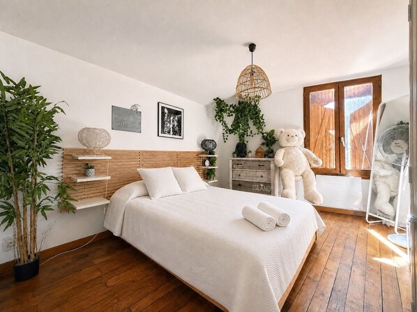 Ein Schlafzimmer mit einem Bett, einem großen Teddybären, einem Ventilator und einer Topfpflanze.