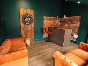 Une pièce avec un jeu de fléchettes, un fauteuil rouge et un comptoir de bar en bois.