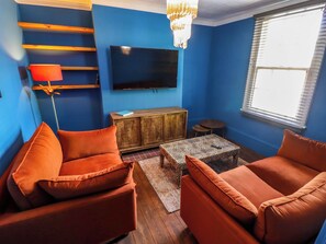 Ein Wohnzimmer mit blauen Wänden, einem Flachbildfernseher, einer Holzkommode und zwei orangefarbenen Sofas.