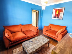 Une pièce avec deux canapés orange, une table basse à motifs léopard et un tableau encadré accroché au mur.