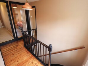 Eine Holztreppe mit schwarzer Geländer, die zu einem Zimmer mit einem Bett und einer Pendelleuchte führt.