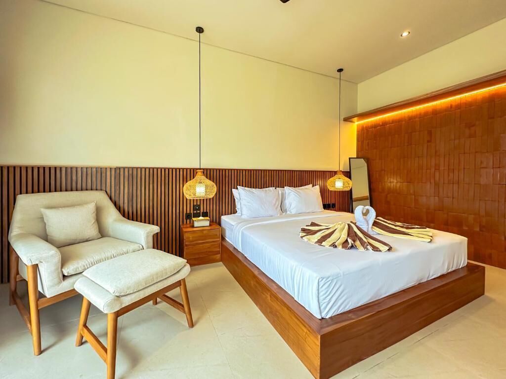 Een moderne slaapkamer met een groot bed, een houten hoofdbord, een nachtkastje met een lamp en een stoel.