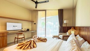 A hotel room with a bed, a desk with a television, a chair, a lamp, and a window with curtains. - Poh Canggu (Badung)
