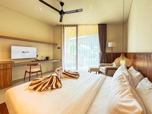 A hotel room with a bed, a desk with a television, a chair, a lamp, and a window with curtains. - Poh Canggu (Badung)