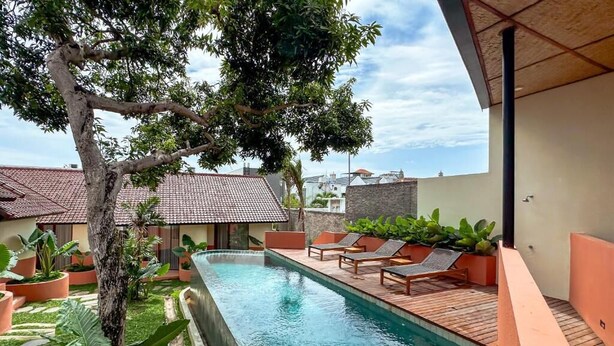 A swimming pool with lounge chairs, surrounded by potted plants and a tree. - Poh Canggu (Badung)