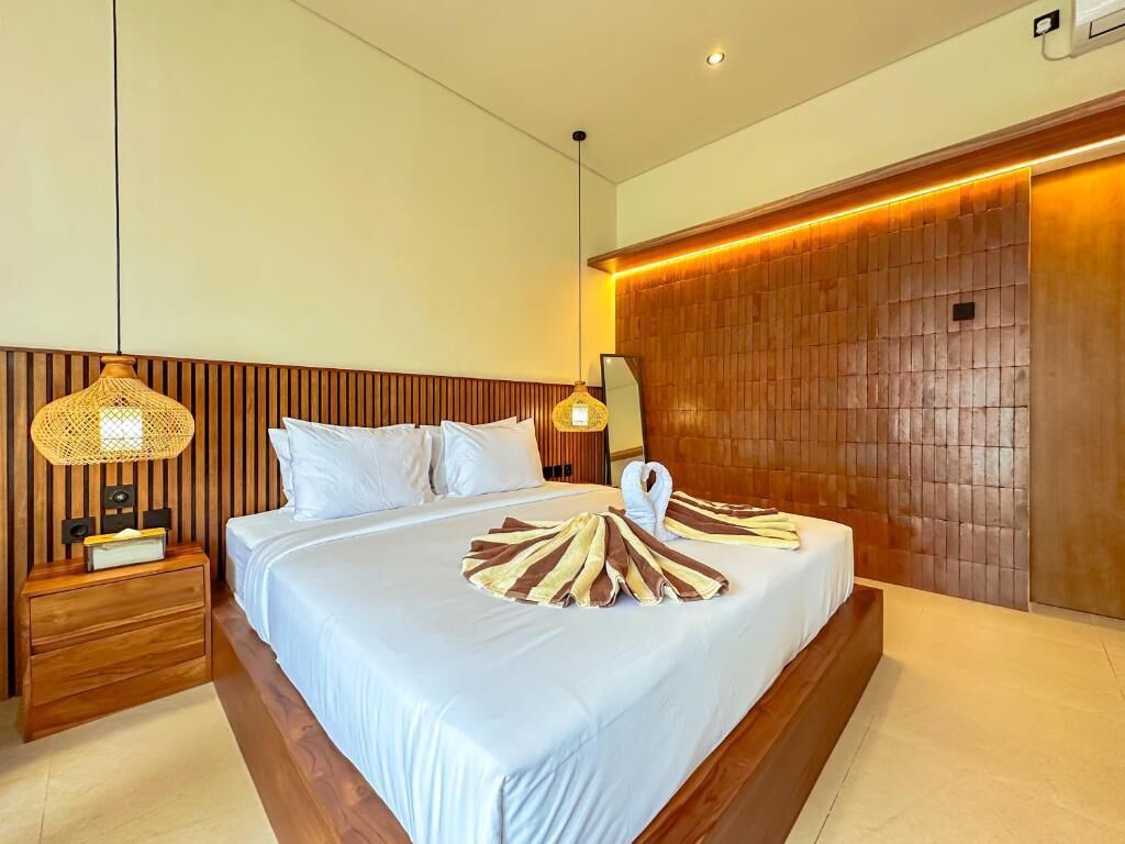 Une chambre d’hôtel avec un grand lit, une tête de lit en bois, des lampes de chevet et un luminaire fixé au mur.