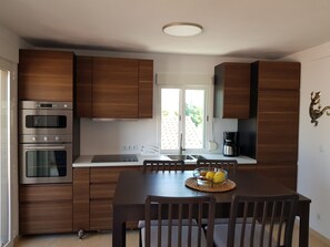 Eine moderne Küche mit Holzausstattung, Edelstahlgeräten, einem Esstisch mit Stühlen und einem Fenster mit Blick auf Grünflächen.