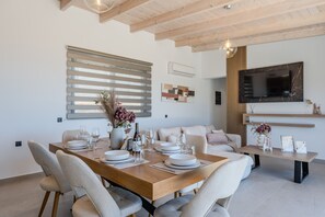 A modern dining area with a wooden table set for four, a sofa, and a TV mounted on the wall. - Rodia Luxury villa ,Sea View Retreat near Plakias (Plakias)