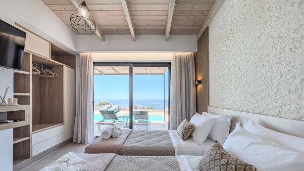 Une chambre avec deux lits, une armoire, une grande fenêtre donnant sur la mer et un plafond avec des poutres en bois.
