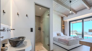 Une salle de bain moderne avec un grand lavabo, une douche et une porte en verre donnant sur une chambre à coucher avec un lit et une vue sur la mer.